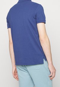 Marinblå polotröja i bomull, med klassisk krage, korta ärmar och sidofrackar i nederkant. Bärs med ljusblå byxor.