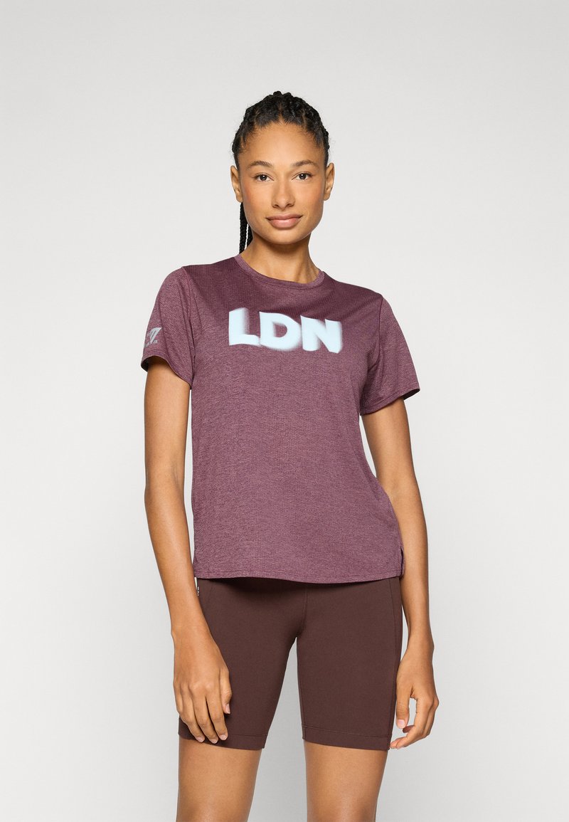 T-shirt atlético de cor bordô com "LDN" em azul claro, mangas curtas, decote redondo e tecido que afasta a umidade. Combinado com calções castanhos.