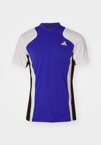 Blauw sportshirt met korte mouwen, met witte en zwarte accenten. Het materiaal lijkt glad met een opstaande kraag en logo-details.