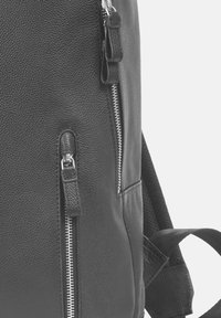 Sac à dos en cuir noir avec un matériau texturé, des fermetures éclair en argent et un design élégant comportant plusieurs poches zippées.