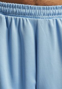 Shorts de sport bleu clair en tissu mesh texturé. Ils présentent une taille élastique froncée, offrant une coupe décontractée.