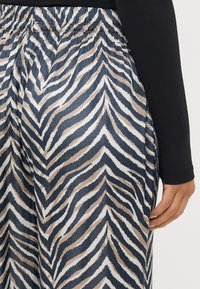 Calças largas em um tecido suave com um padrão de zebra em zig-zag nas cores creme, bege e azul escuro, e com cintura elástica.