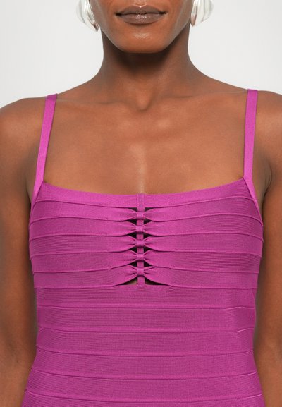 Top corto fucsia con texture a coste, spalline sottili e dettagli frontali con sezioni arricciate che creano un effetto ondulato visivo.