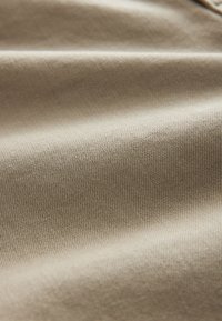Gros plan d'un tissu beige avec une texture fine en tricot et des plis doux montrant des ombres subtiles et des détails.