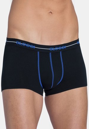 Man die zwarte boxershorts draagt met blauwe stiksels en een zwarte tailleband met blauwe "Sloggi"-logo's, tegen een witte achtergrond.