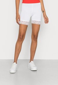 Vita stretchshorts med spetskant i fållen, kombinerade med vita sneakers. Designen är figurnära med en slät yta och en längd till mitten av låret.
