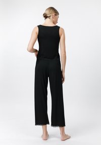 Schwarzes ärmelloses Top mit rundem Halsausschnitt, kombiniert mit weiten schwarzen Hosen, die am Saum mit zarter Spitze veredelt sind. Weiche Stofftextur.