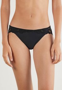 Zwarte bikini broek met kantafwerking aan de taille, zachte stof, lage taille en naadloze randen voor een comfortabele pasvorm.