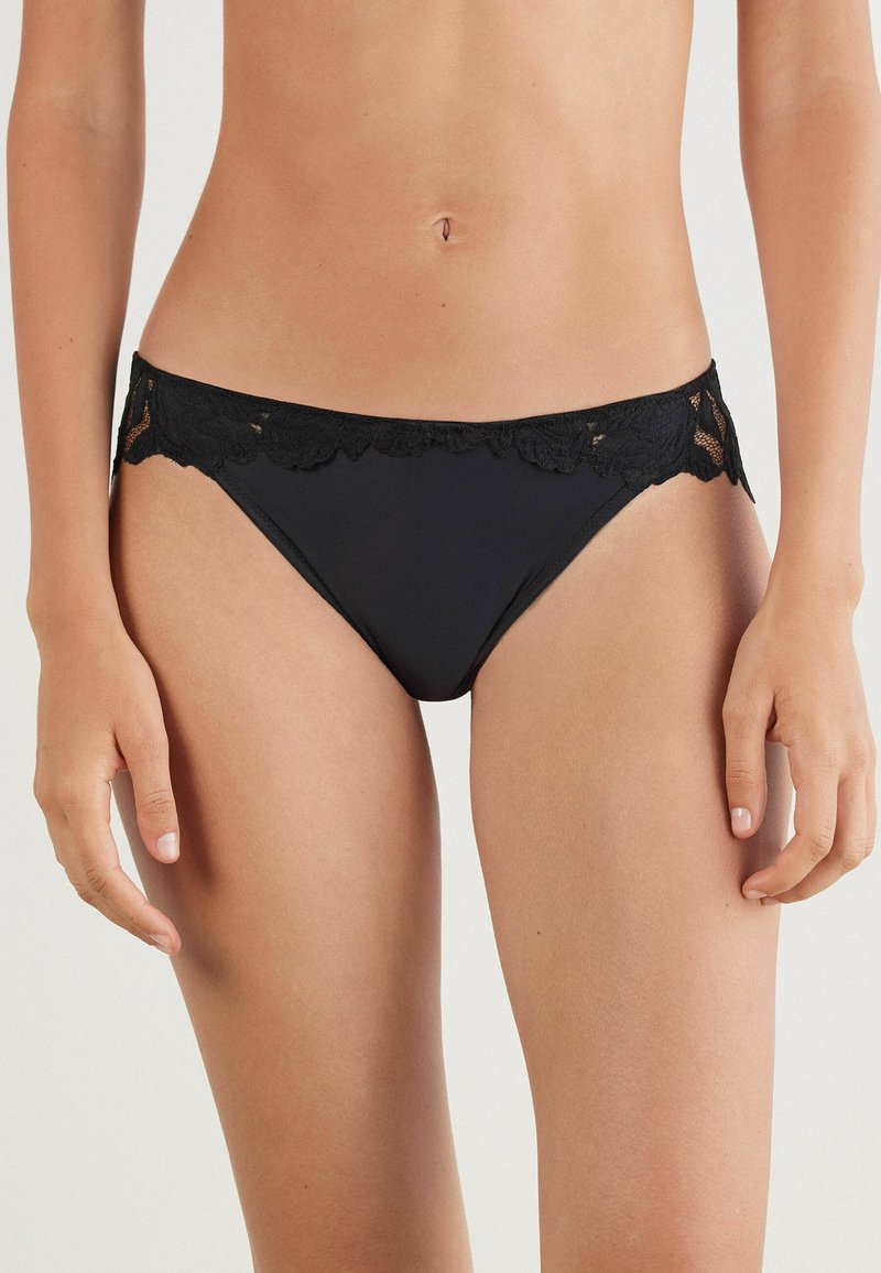 Zwarte bikini broek met kantafwerking aan de taille, zachte stof, lage taille en naadloze randen voor een comfortabele pasvorm.