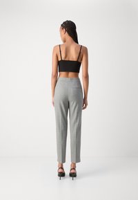 Un haut court noir et un pantalon à carreaux gris, présentant une coupe ajustée, des jambes droites, des poches et une texture subtile, associés à des talons noirs.