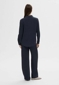 Navy blue long-sleeve shirt with a collar, paired with matching wide-leg trousers. Soft fabric, relaxed fit, and rounded hem detail on the shirt.