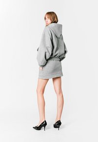 Sudadera con capucha gris combinada con una minifalda a juego. El conjunto presenta un ajuste relajado, bordes acanalados y zapatos de tacón negro.