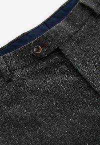 Pantalones de mezcla de lana gris con una textura moteada. Presentan una cinturilla puntiaguda, cierre de botón y forro interior azul marino.