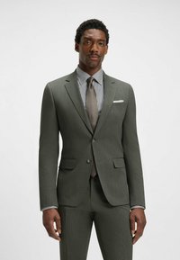 Dark green suit made of textured fabric, featuring a fitted blazer, notch lapels, and slim trousers. Paired with a striped shirt and tie.