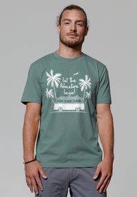 Korte mouwen teal t-shirt met een witte afbeelding van een busje met palmbomen en de tekst "Laat het avontuur beginnen!" in een informele lettertype.