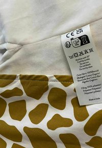 Cieta un poliestera spilvendrāna ar baltu pamatu un lielām dzeltenīgi sinepju krāsas neregulārām formām. Pielikta kopšanas etiķete ar mazgāšanas instrukcijām.