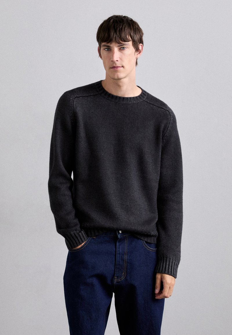 Dark gray knitted sweater with a round neckline, ribbed cuffs and hem, paired with dark blue denim pants. Smooth texture, relaxed fit.