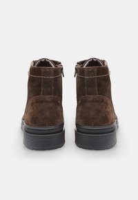 Botas de tobillo de ante marrón con acabado texturizado, que presentan cremalleras a los lados y una suela de goma negra estriada para mayor agarre.