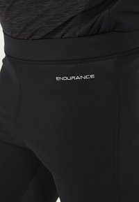 Svarta tights i åtsittande modell, tillverkade av stretchigt material. Har en mjuk yta med en vit logotyp "ENDURANCE" på sidan. Inga mönster eller synliga detaljer.