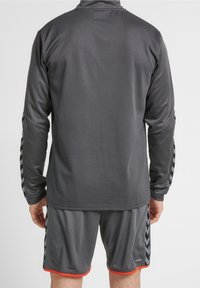 Giacca sportiva grigia con un motivo testurizzato, maniche lunghe e dettagli a zigzag neri sui lati, abbinata a pantaloni corti coordinati.