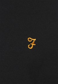 Tejido de punto negro con una 'f' estilizada en naranja bordada en la esquina inferior. Textura suave con un peso medio.