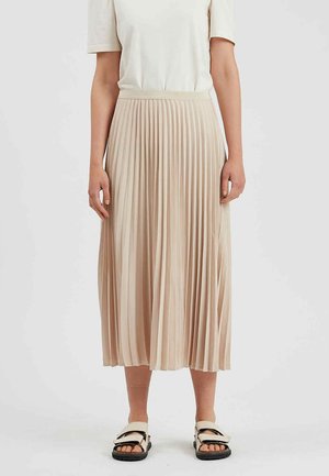 Femme portant un haut blanc à manches courtes, une jupe midi plissée beige et des sandales beiges avec semelles noires sur fond blanc.