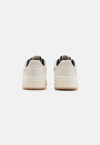 White suede sneakers with a textured finish, contrasting black accents, and a thick rubber sole featuring a gum color.