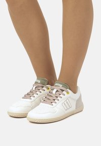 Weiße Sneakers mit glattem Lederobermaterial, beigen Akzenten, grauer Ferse und hellgrauen Schnürsenkeln. Mit perforierter Zehenpartie und Logo auf der Zunge.