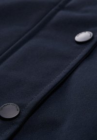 Tumši jūras flīsa audums ar gludu tekstūru, redzamu šuvju un diviem matētiem melniem pogām. Viens poga parāda "DENIM TOM TAILOR" zīmolu.