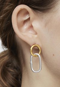 Pendientes de metal en oro y plata que presentan un aro redondo de oro y un diseño de eslabón ovalado en plata, mostrando una superficie suave y brillante.