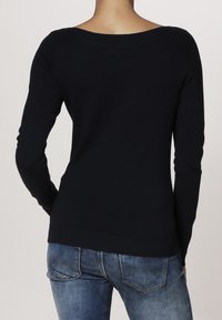 Dunkelblauer Longsleeve-Pullover aus weichem Strickmaterial, mit weitem Rundhalsausschnitt und taillierter Silhouette, kombiniert mit hellblauen Denim-Jeans.