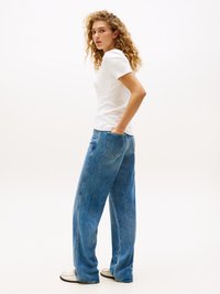 Hvid kortærmet skjorte parret med lyseblå vide jeans. Sættet har en afslappet pasform og er suppleret af en neutral baggrund.
