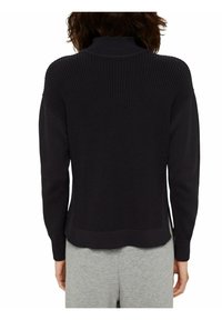 Maglione lavorato a maglia blu navy scuro con collo alto, texture a costine e maniche scese. Presenta un orlo cropped e spacchi laterali.