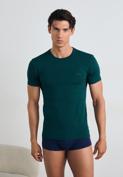 T-shirt vert à manches courtes en tissu doux avec un col rond et un logo discret sur la poitrine gauche, accompagné de boxer bleus marine.