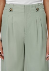 Light green pleated trousers featuring a smooth fabric, two front buttons, and side pockets. Tailored design with a relaxed fit.