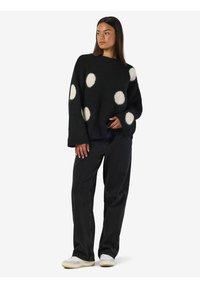 Suéter negro y peludo con grandes lunares blancos y mangas anchas, combinado con pantalones rectos negros y zapatillas blancas.