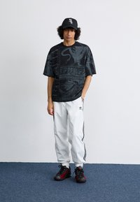Svart grafisk t-skjorte med abstrakte design, kombinert med hvite joggebukser med side-striper og svarte/røde joggesko.
