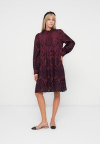 Maroon embroidered dress with long sleeves, intricate cut-out patterns, and a flared hem. Worn with nude and black flats.