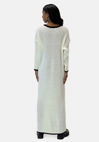 Langer gerippter Pullover in Weiß mit schwarzen Akzenten am Kragen und Saum, mit weit geschnittenen Ärmel und einer lockeren Passform, aus einem gestrickten Material gefertigt.