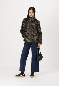 Manteau en fausse fourrure imprimé léopard avec col montant, associé à un pantalon en denim à jambes larges et des baskets noires. Petit sac à main noir avec chaîne.