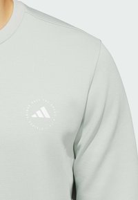 Felpa verde chiaro con logo Adidas bianco rotondo e testo, colletto a coste e superficie liscia.
