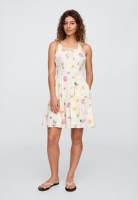 Vestido de verão com padrão floral em creme, apresentando corpete justo, alças ajustáveis e saia em camadas. Feito de tecido leve.