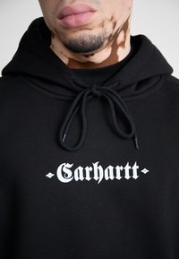 Felpa nera con cappuccio in cotone con coulisse e logo frontale bianco. Presenta un tessuto strutturato e maniche con risvolto ben evidenti.