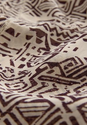 Tessuto di cotone con intricati motivi geometrici marroni su sfondo beige, caratterizzato da una texture liscia e pieghe fluide.