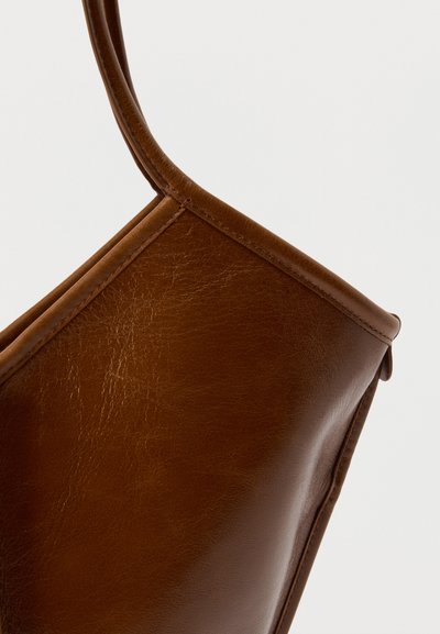 Καφέ δερμάτινη τσάντα tote με λεία υφή, γωνιαίο σχήμα και ανθεκτικούς, στρογγυλεμένους ιμάντες. Διακριτά ραφές κατά μήκος των άκρων.