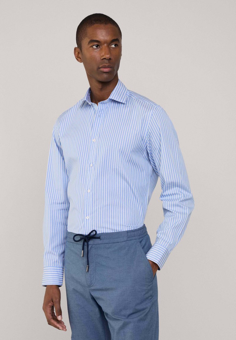 Camicia a manica lunga blu e bianca a righe con colletto a abbottonatura, realizzata in un morbido misto cotone e con un design slim fit. Abbinata a pantaloni blu con cordino.