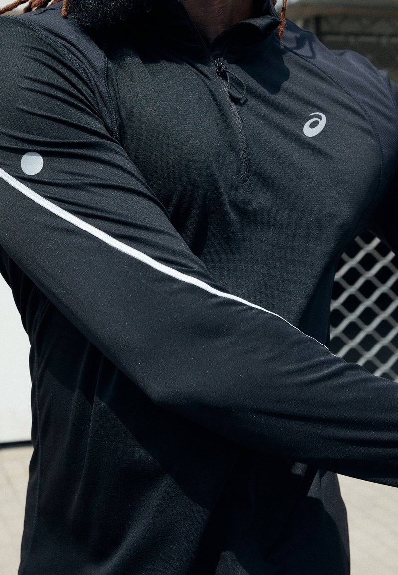 Czarny, zapinany na zamek sportowy top wykonany z teksturowanej tkaniny. Posiada biały pasek na rękawie oraz okrągły akcent na ramieniu.