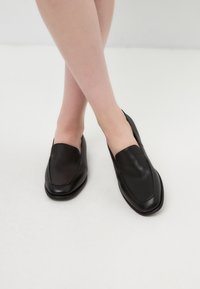 Black leather loafers with a square toe, featuring a smooth finish and minimalistic design, resting on a light background.