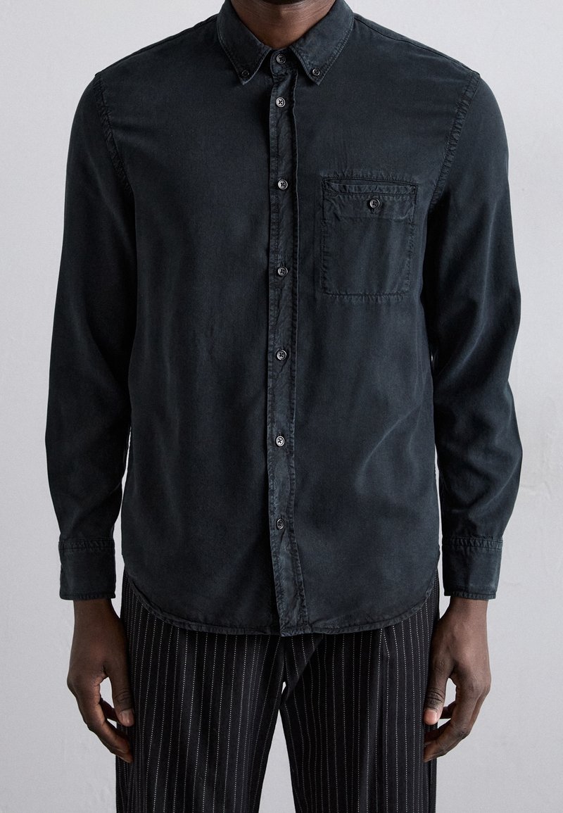 Camicia nera con bottoni, con taschino, maniche lunghe, in tessuto morbido e vestibilità casual, abbinata a pantaloni neri a righe.