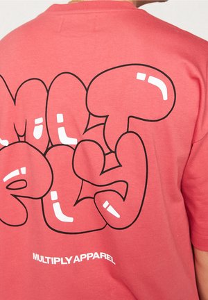 Tył koralowej koszulki z dużą, bąbelkową grafiką z czarnym konturem i białym napisem "MULTIPLY APPAREL" w pobliżu brzegu.